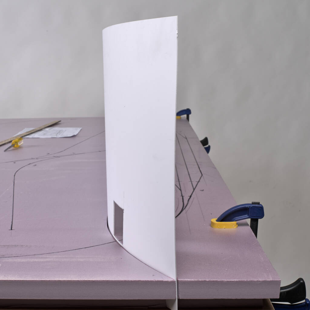 Color photo showing white styrene sheet used as backdrop on unfinished model railroad.