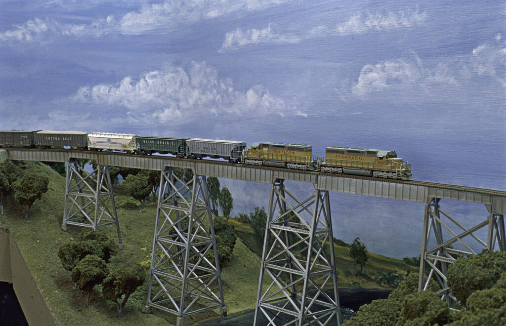 A model train crosses an elevated bridge on a model railroad layout