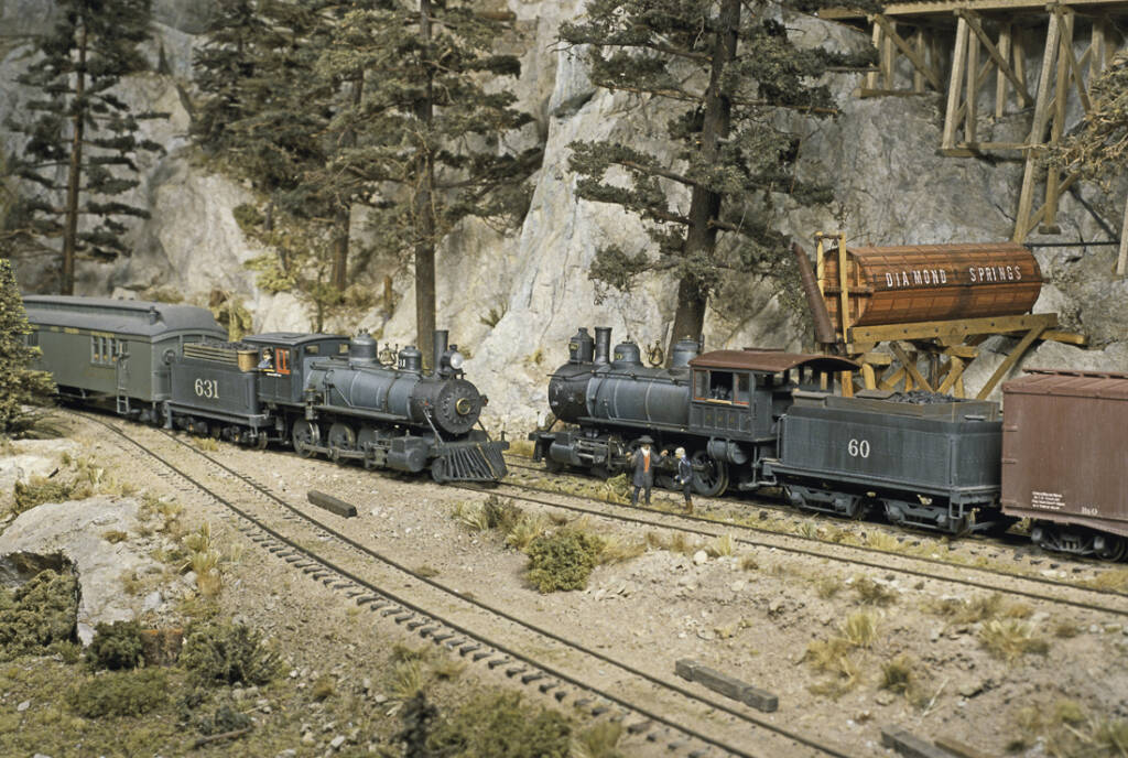 Two steam trains approach each other on a model railroad layout