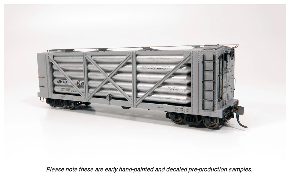 Gray and silver model train freight car with black wheels, brown couplers, and open sides displaying long silver tubes laying on their sides.