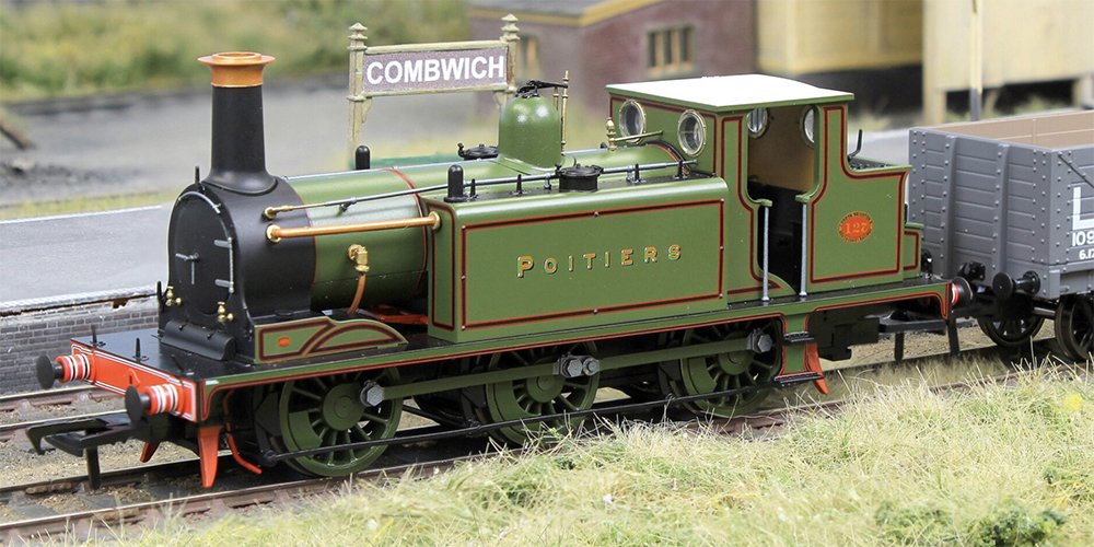 Green, black, red, and white model train steam locomotive shown from the side with round windows in its cab and 3 pairs of larger driving wheels painted green.
