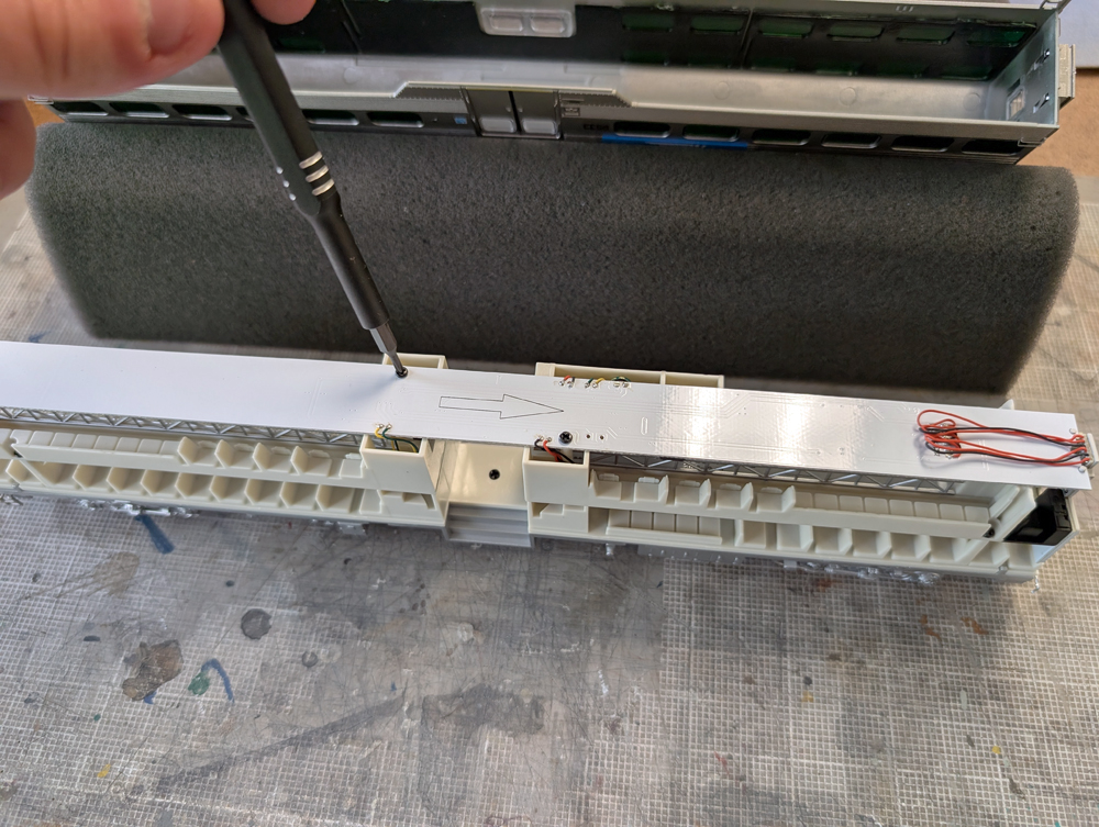 A screwdriver unscrewing screws at the top of an HO scale passenger car's interior