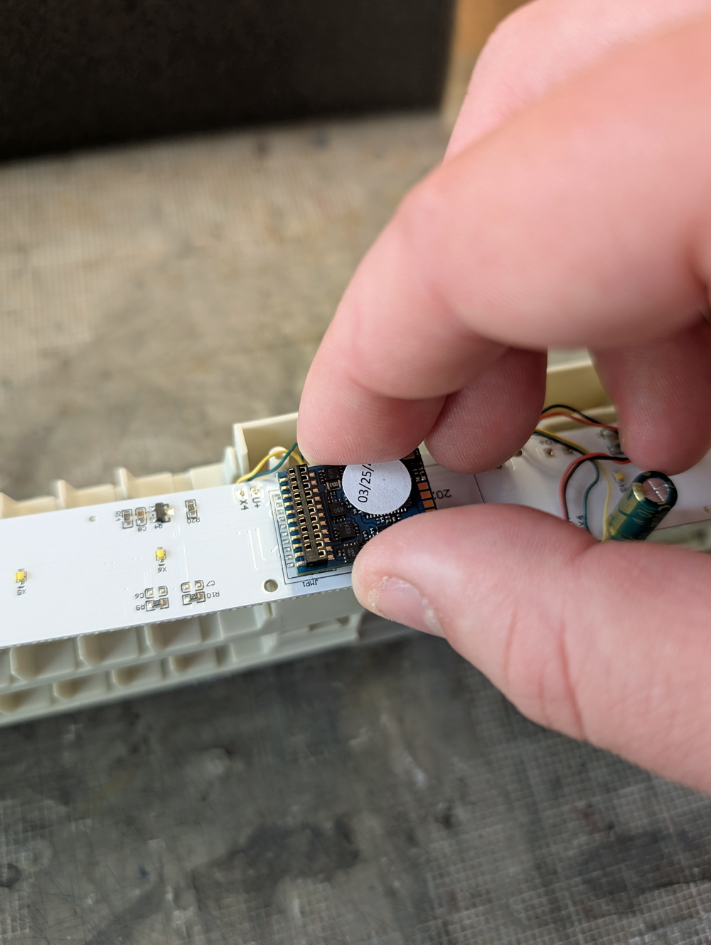 Two fingers placing a DCC decoder on pins