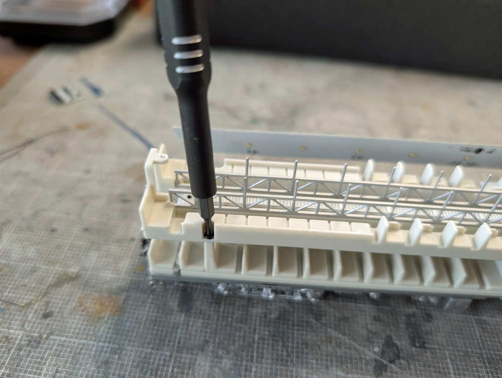 A screwdriver unscrewing the top floor of an HO scale passenger car