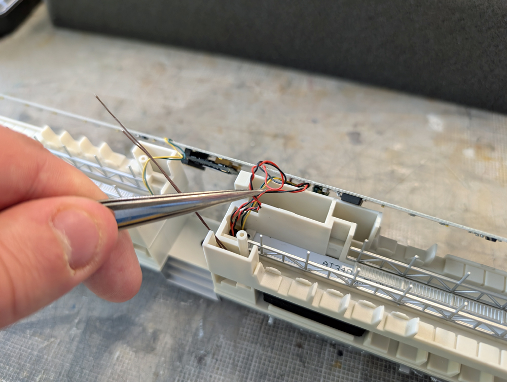 A hand with tweezers holding wires of an HO scale passenger car