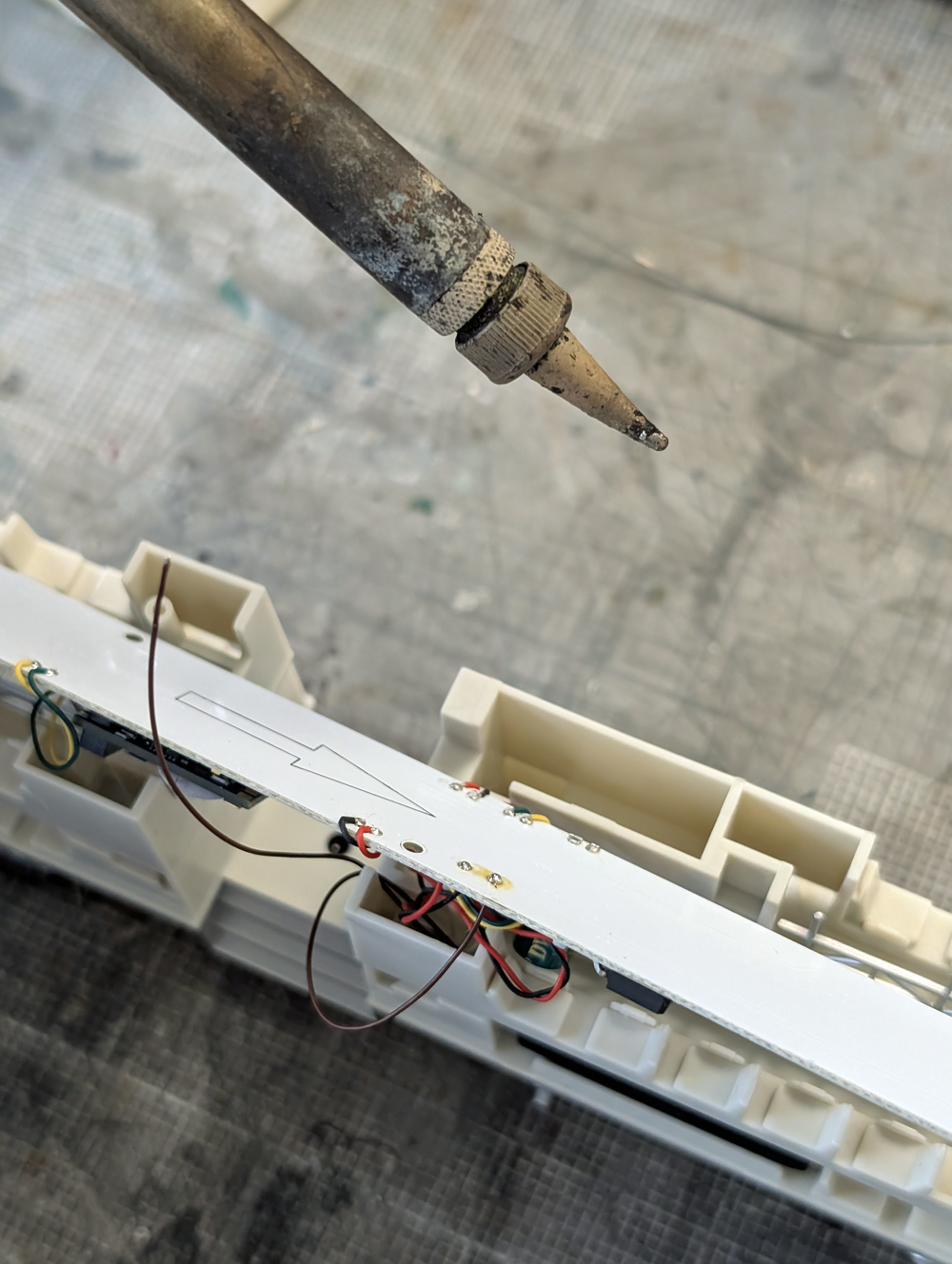 A soldering iron above a light board after soldering wires to it.