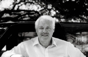 Man with mustache in white shirt under trees
