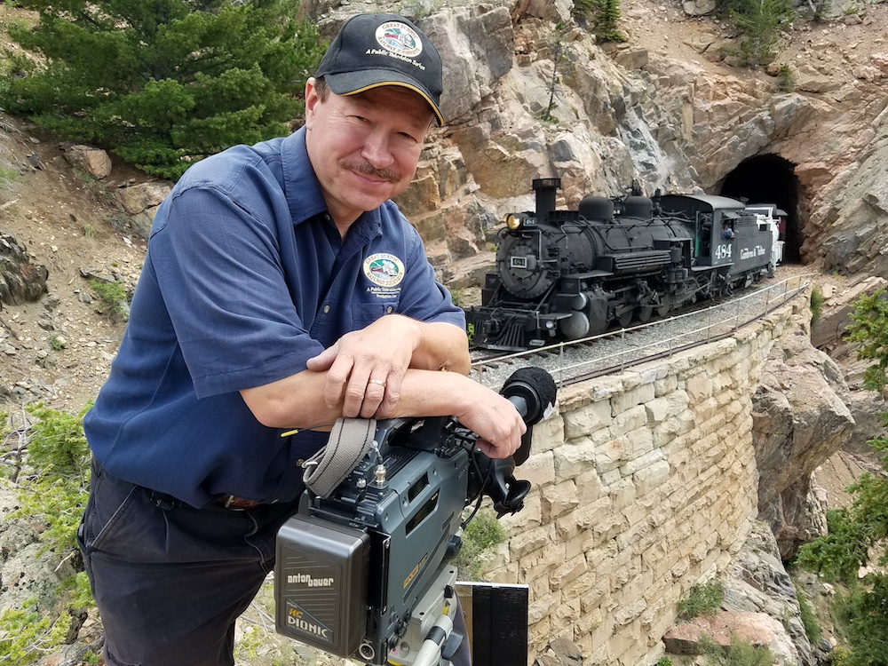 Man posing with camera in front of steam locomotive