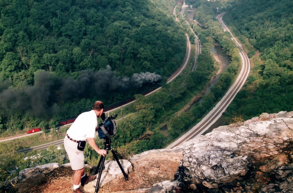 Cameraman filming steam train from cliff