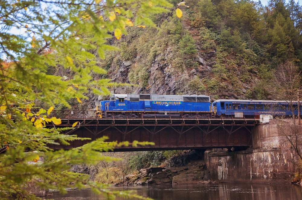 Blue diesel locomotive on passenger train crossing bridge