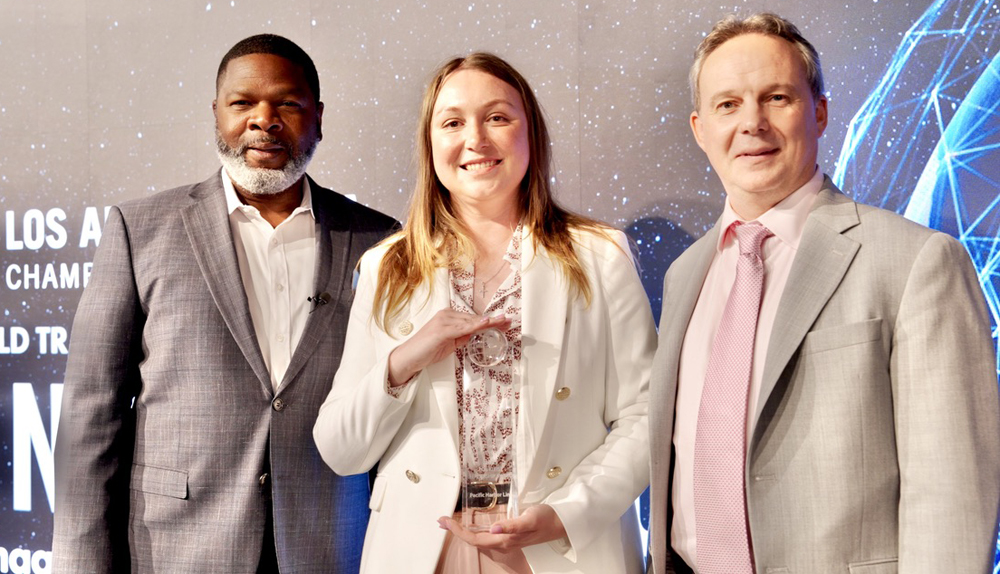 Three people standing, with woman in center holding glass trophy