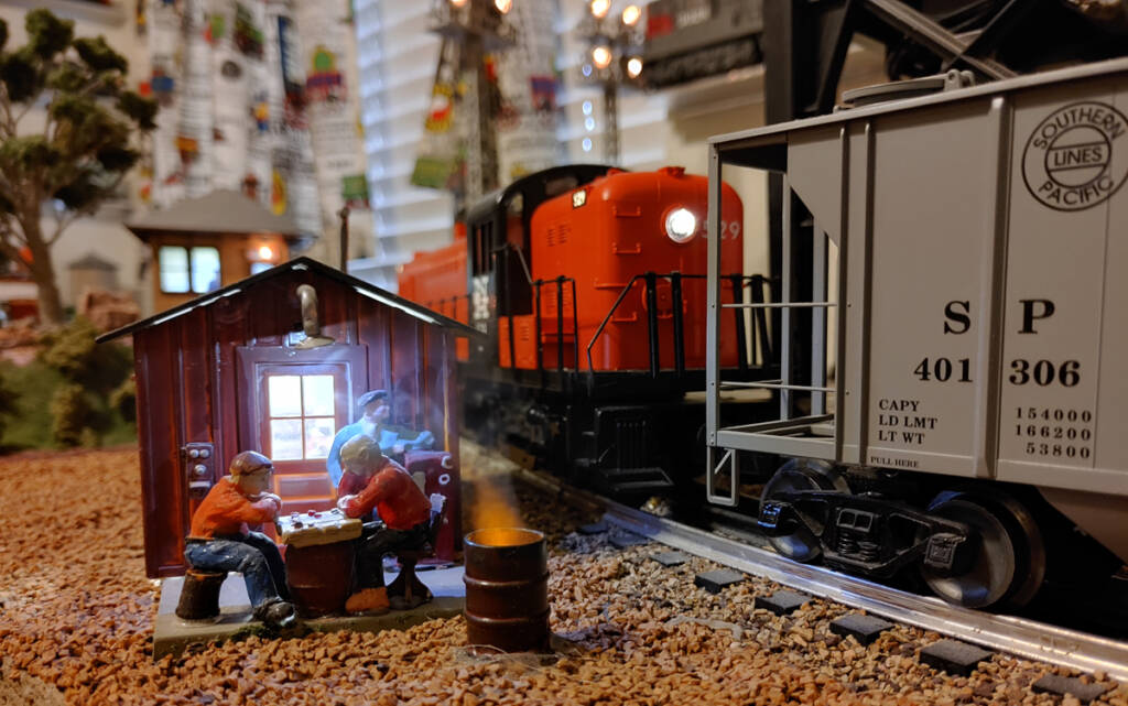 Two model figures sit next to a fire barrel on a toy train layout