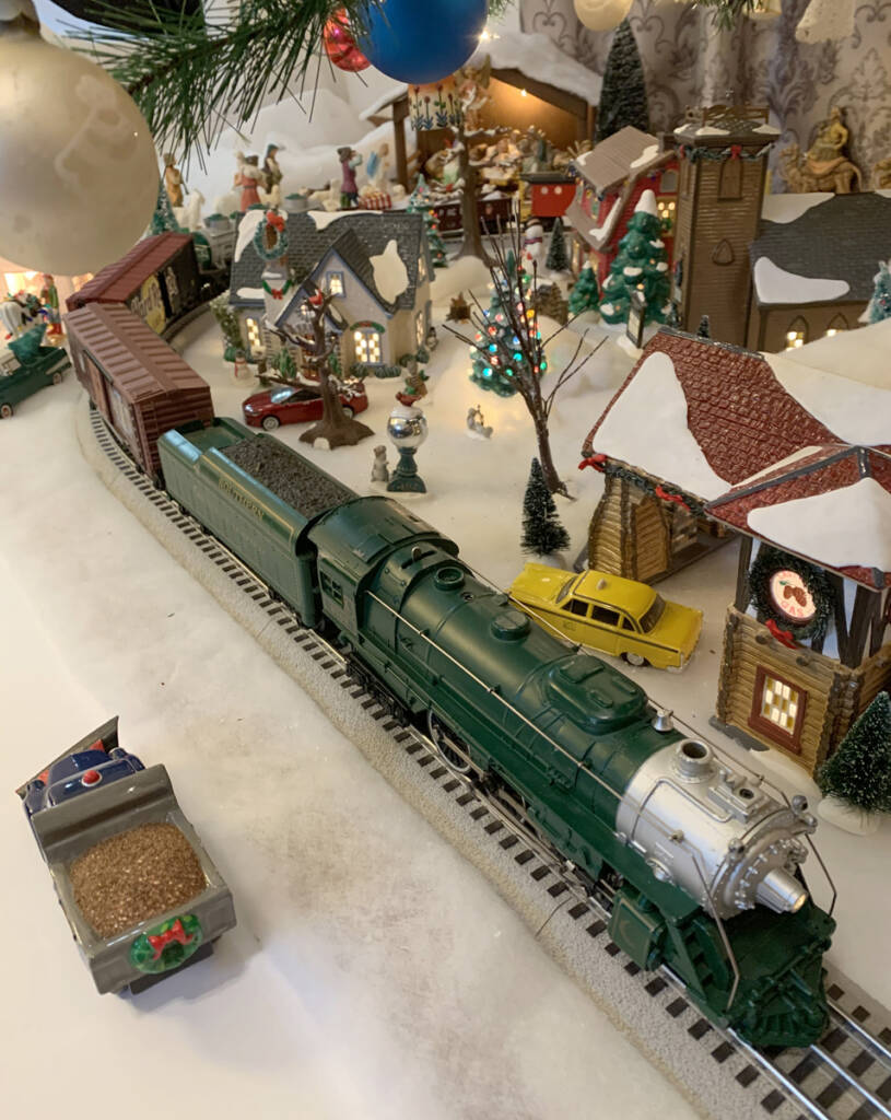 A green toy locomotive leads a toy train on a toy train layout