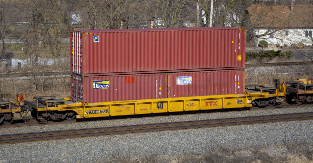 Color photo of yellow 40-foot well car with three mineral red intermodal containers.