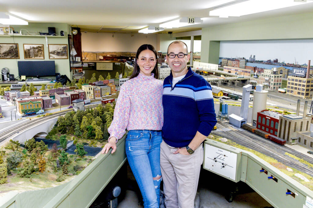 A man and a woman stand in front of a large model railroad layout