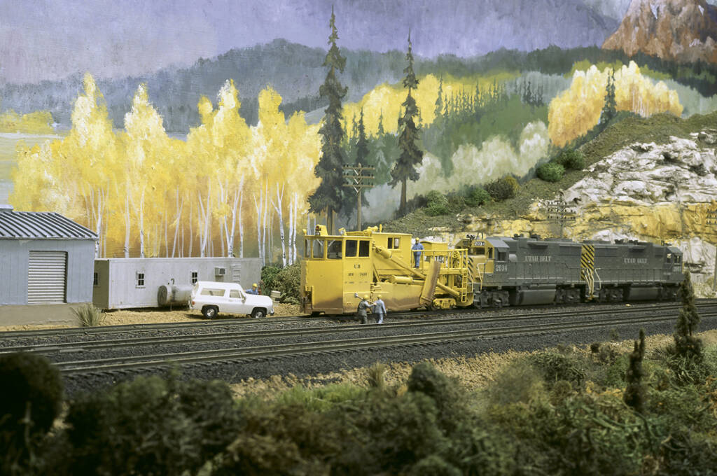 A yellow locomotive on a model railroad layout with yellow and green foliage in the background