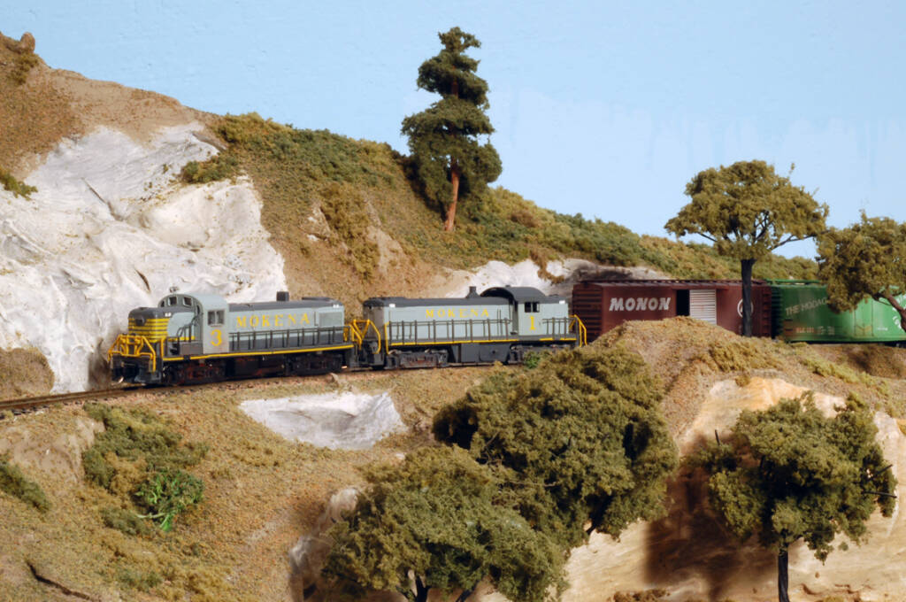 Two gray and yellow model locomotives lead a train on. model railroad layout