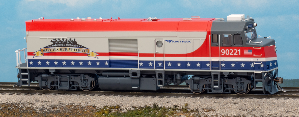 Color photo of HO scale diesel locomotive painted silver with red, white, and blue stripes on scenicked base.