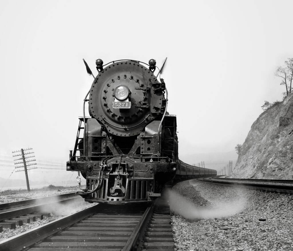 A New York Central Hudson class steam locomotive with a hill on the right and the Hudson River on the left.