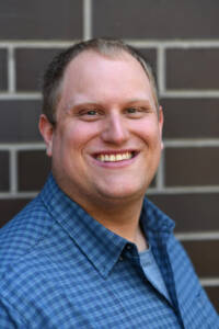 A man in a blue shirt standing in front of a brick wall