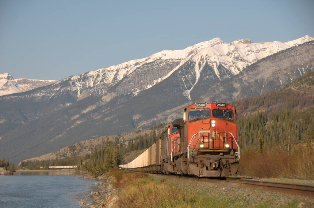 Coal train with two locomotives running next to river with Canadian Rockies as a backdrop