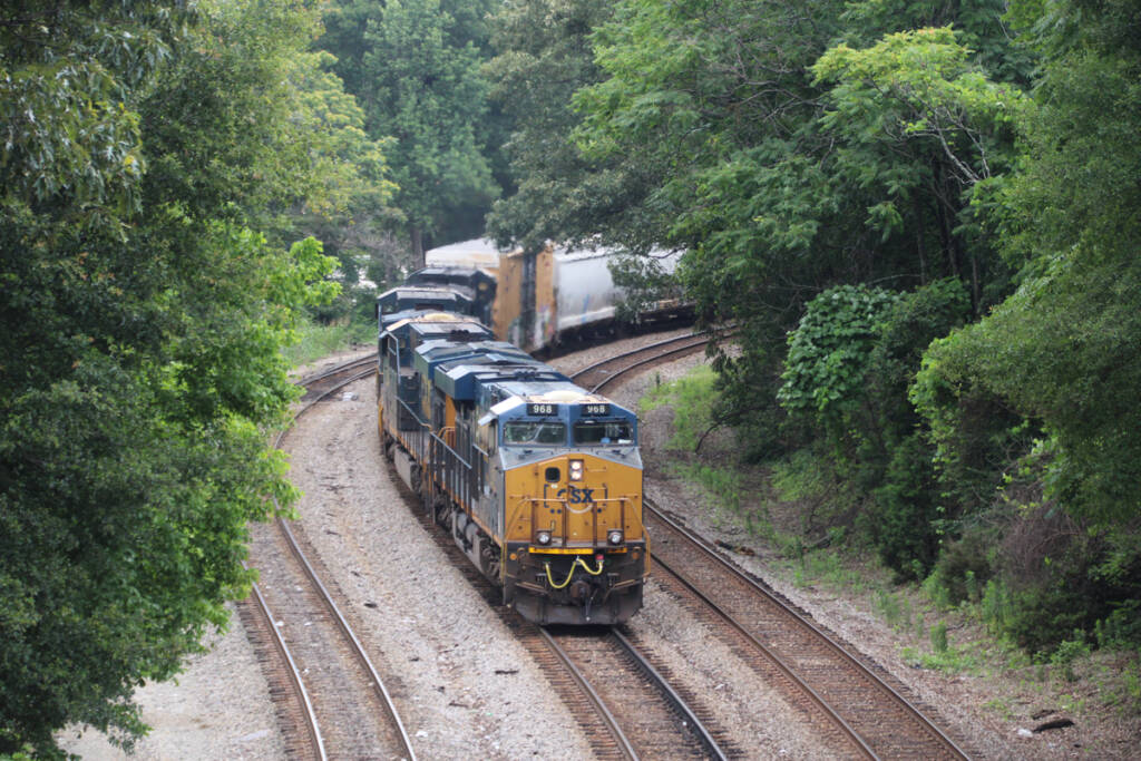 Freight train with blue and yellow locomotives on three-track line surrounded by trees