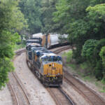 Freight train with blue and yellow locomotives on three-track line surrounded by trees