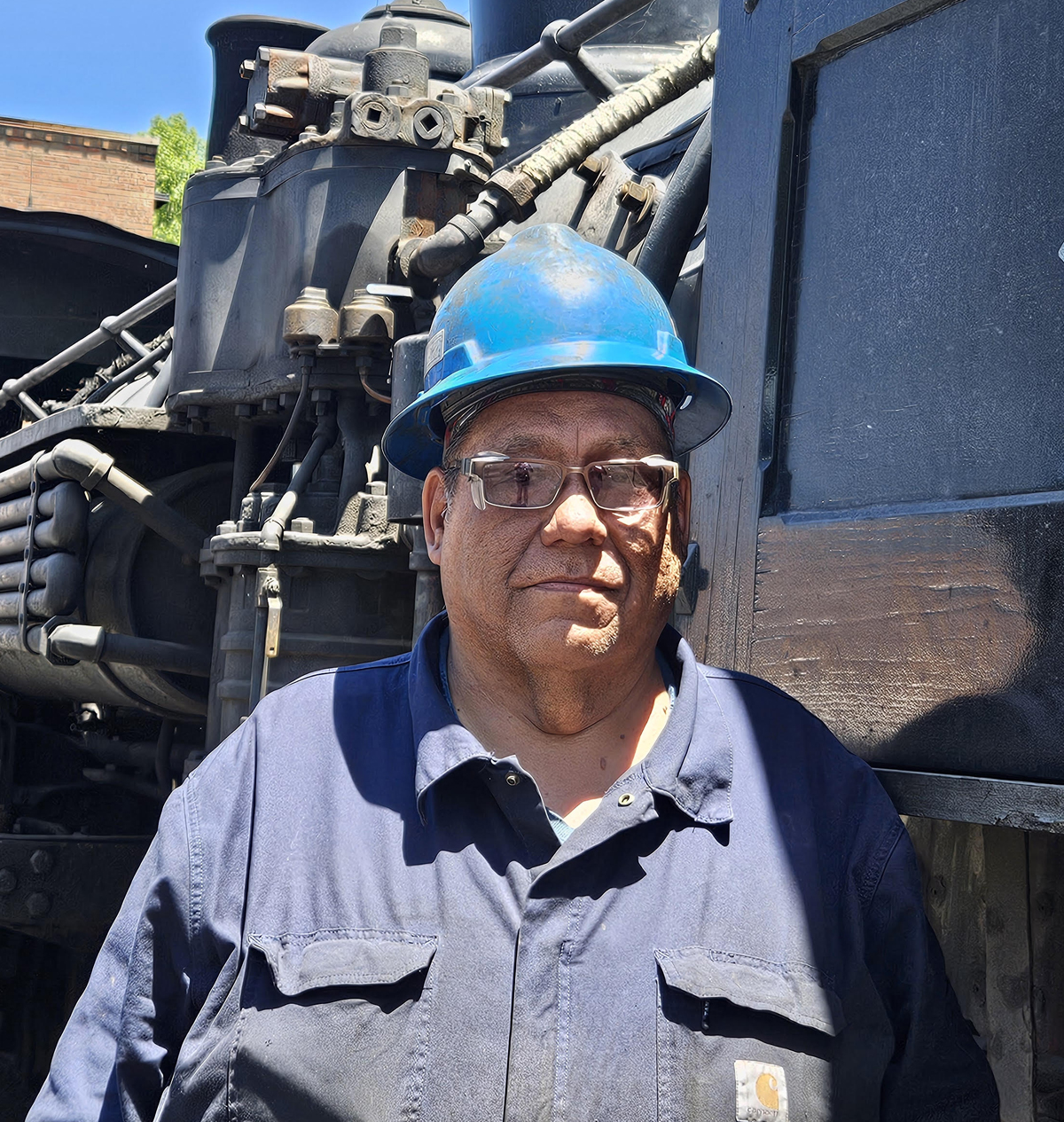 Man in hard hat standing next to steam locomotive