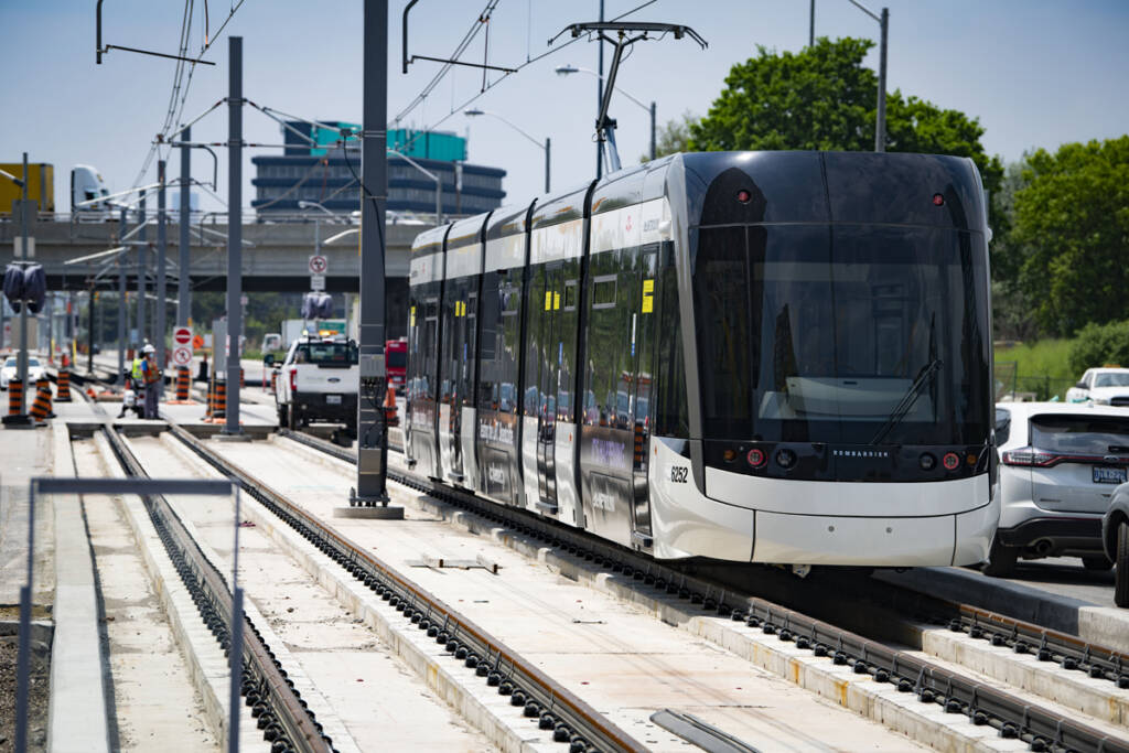 Black and white light rail trainset on track with construction work visible in background