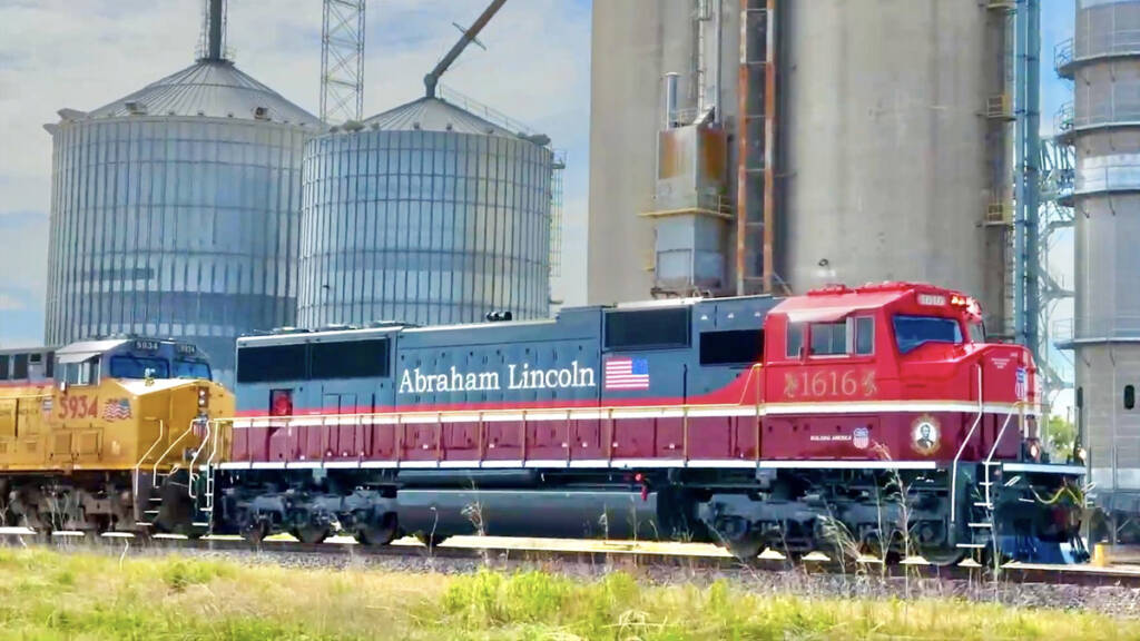 Red, maroon, and gray locomotive passing grain elevator