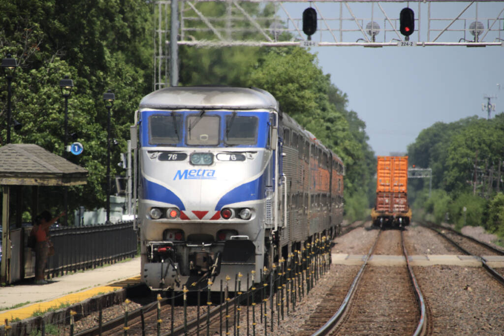 Commuter train in push mode departs station as freight train moves away on adjacent track
