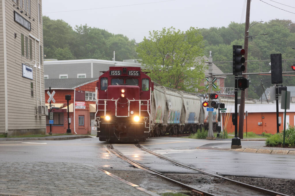 Train with red locomotive and covered hoppers curves through town