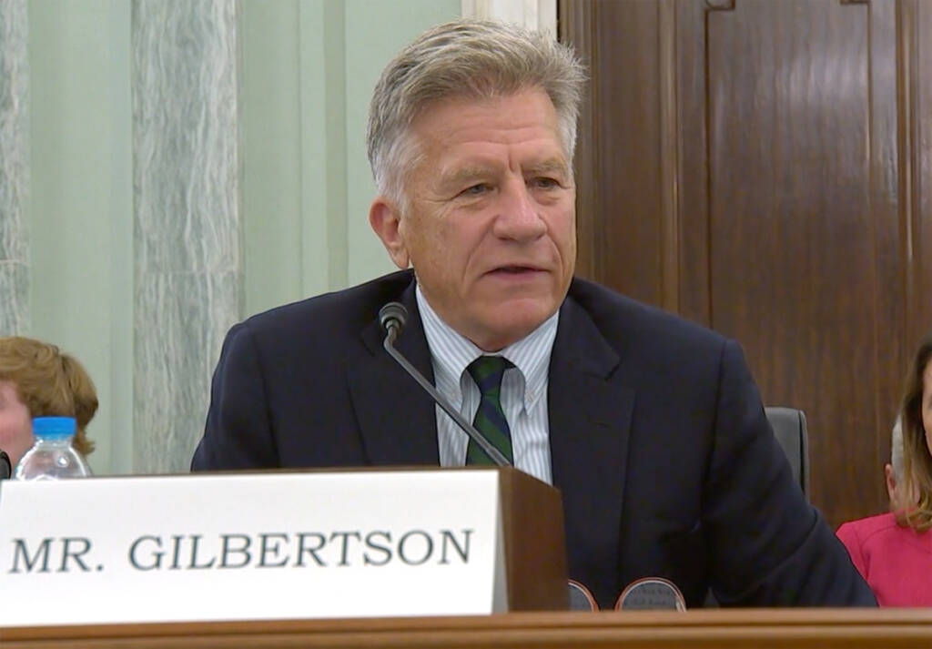 Man speaking in hearing with name plate ("Mr. Gilberson") in foreground