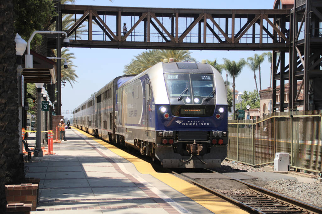 Passenger train passes under pedestrian bridge at station