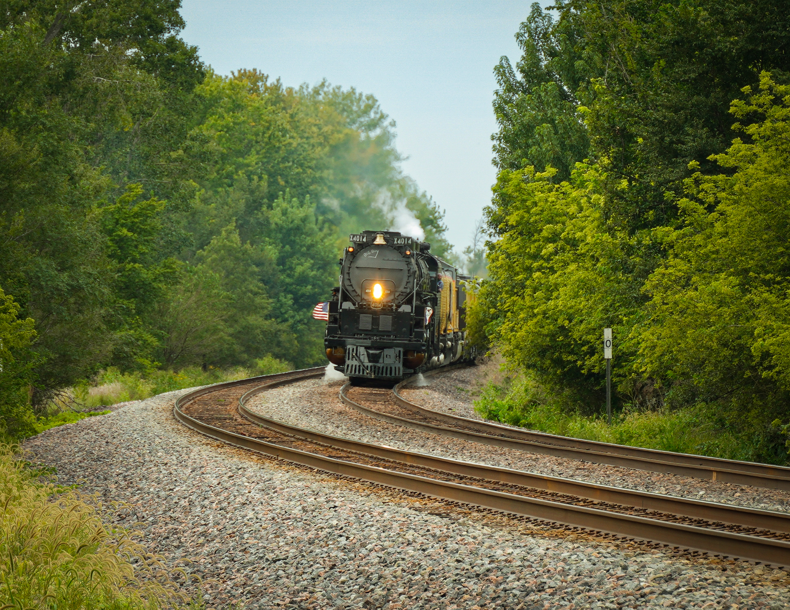 Big steam locomotive rounds curve during late summer