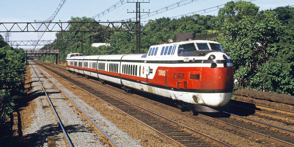 White, red, and blue passenger train at speed under signal bridge