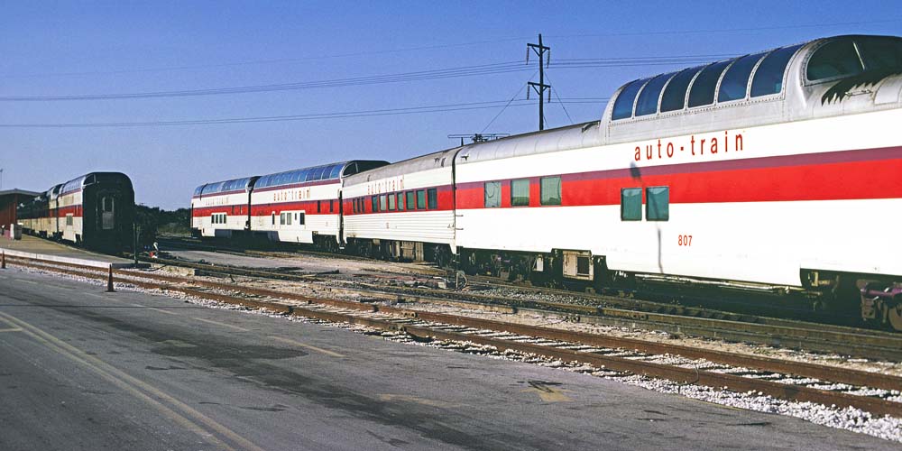 White, red, and purple passenger train cars in yard