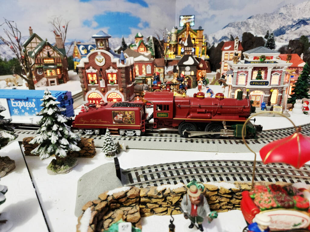 A winter scene on a toy train layout with a toy red steam loocmotive