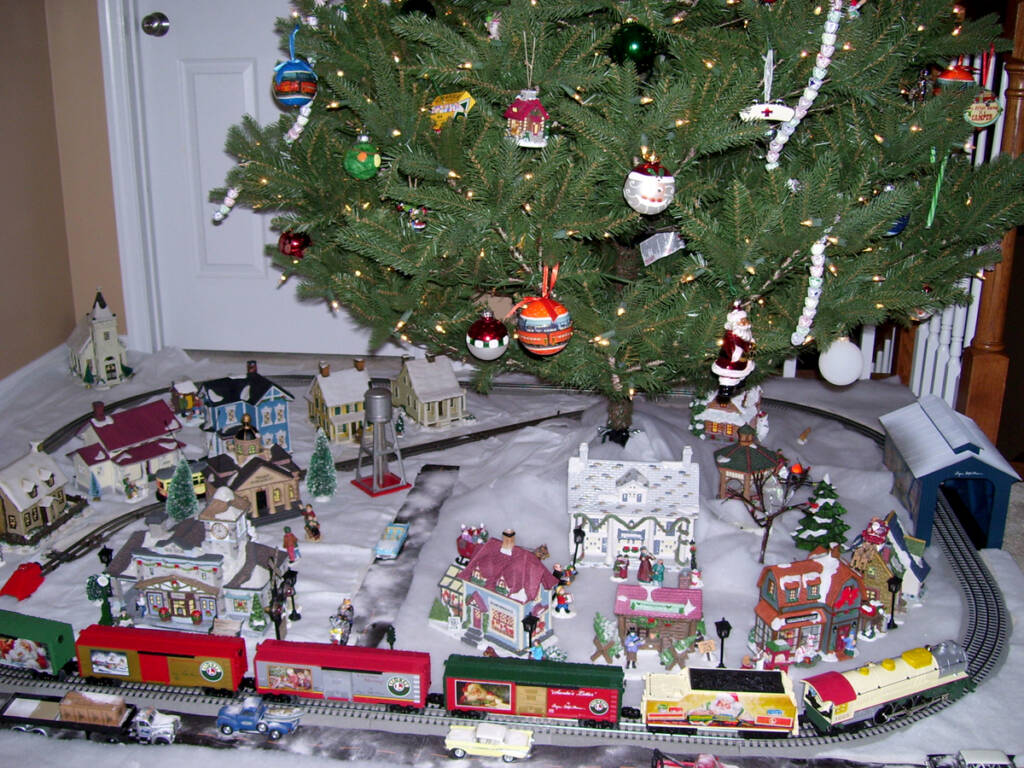 A toy train layout assembled around the base of a Christmas tree