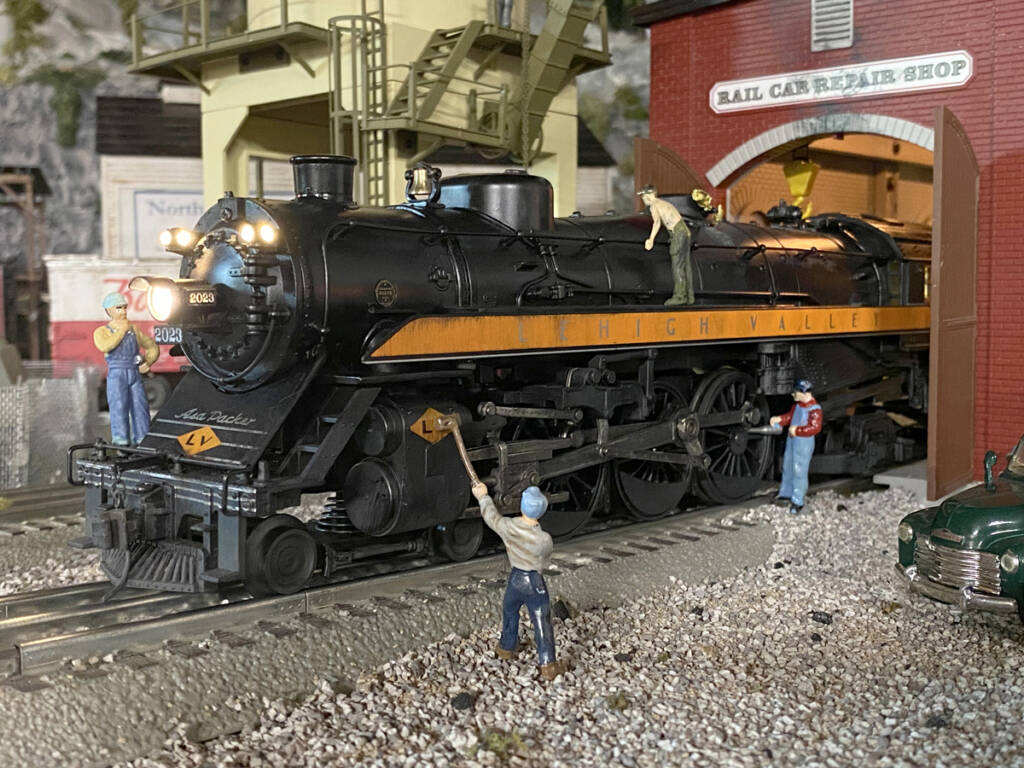 A toy train locomotive exiting a structure near toy figures on a toy train layout