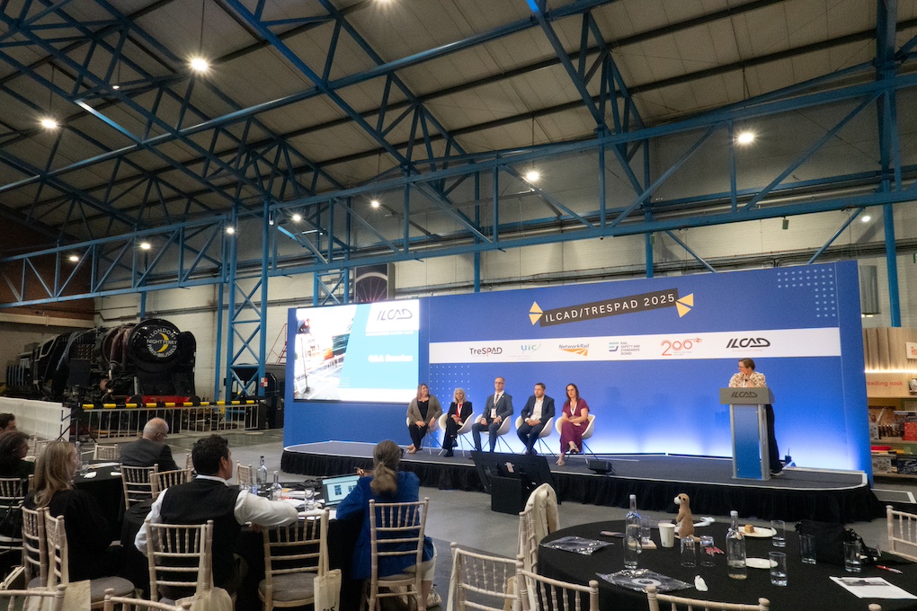 In front of a blue backdrop lettered ILCAD/TRESPAD 2025, a six-person panel discusses rail safety for an audience seated in the exhibit hall of the National Railway Museum in York, United Kingdom
