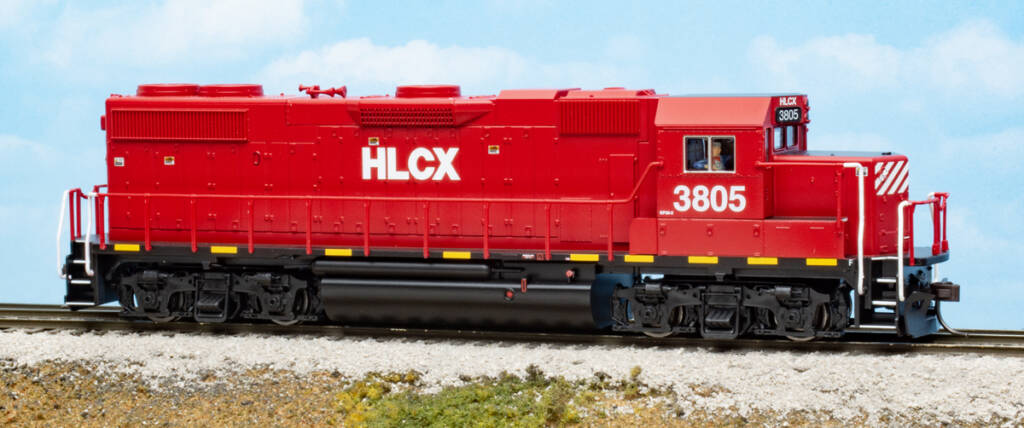 Color photo of HO scale four-axle hood unit painted crimson and black with white lettering and yellow stripes on scenicked base with clouds in background.