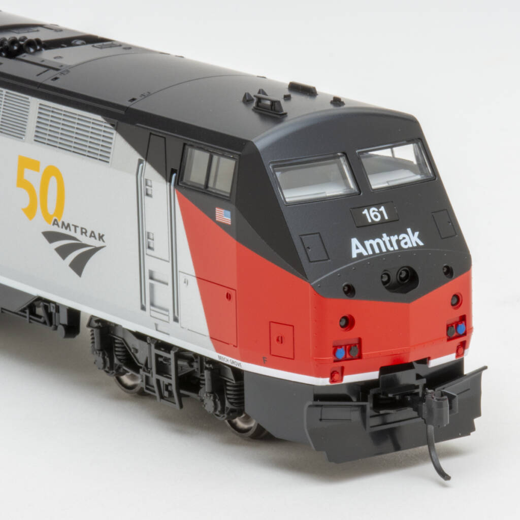 Color photo showing front of modern streamlined HO scale passenger diesel painted red, silver, and black with red, blue, black, and yellow graphics on white background
