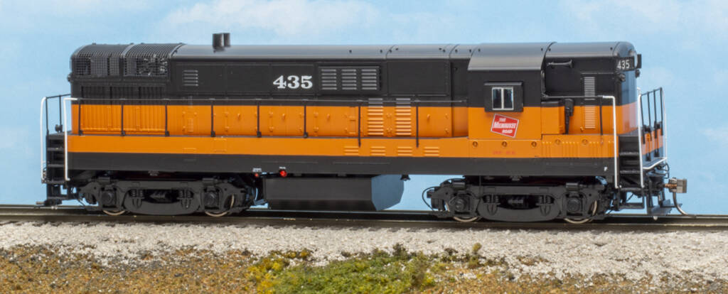 Color photo of HO scale diesel painted orange and black on scenicked base 