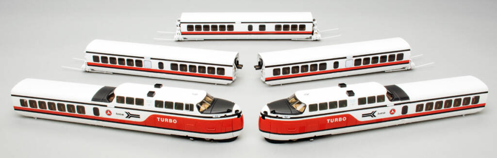 Color photo of five individual red, white, and black toy passenger train cars spread out on a gray paper background.