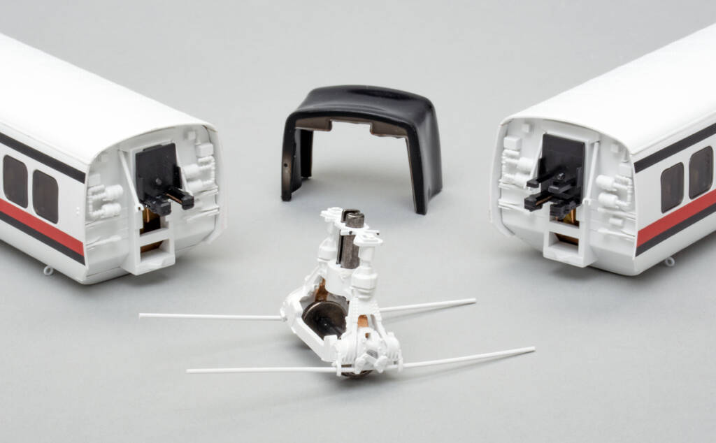 Two red, white, and black toy train passenger cars disassembled and displayed with a white and silver single-axle truck and black plastic U-shaped diaphragm that fits between the two cars.