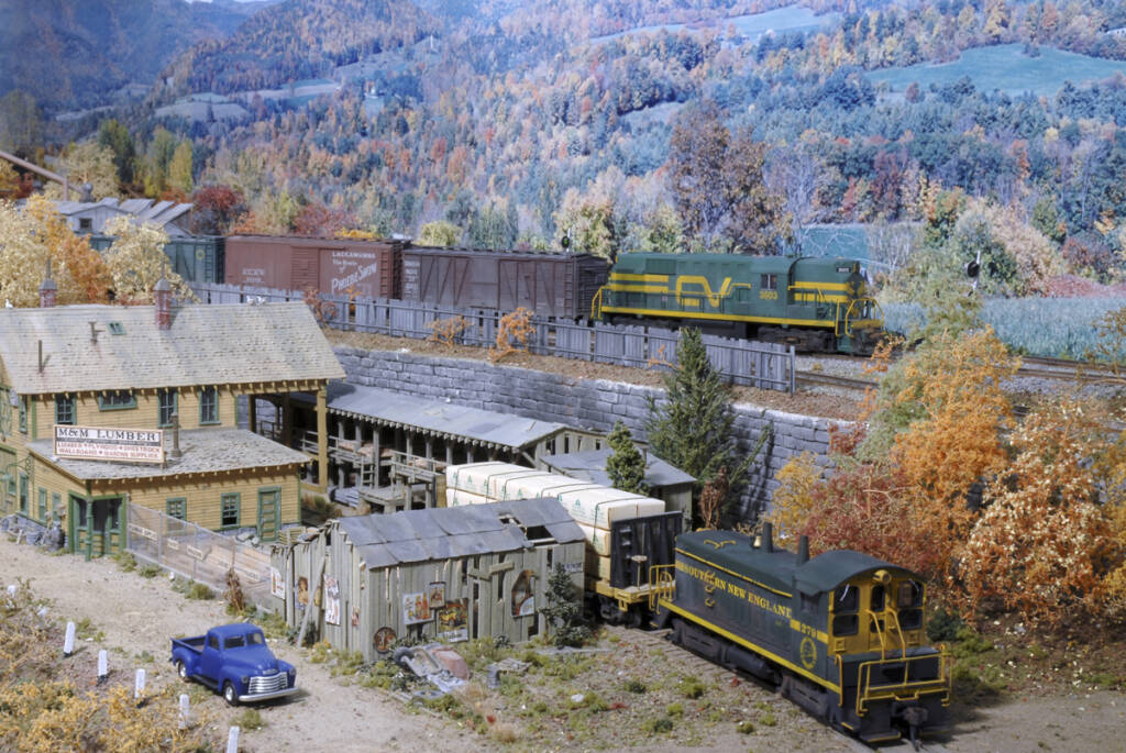 A model railroad layout with multiple trains running in an autumnal setting