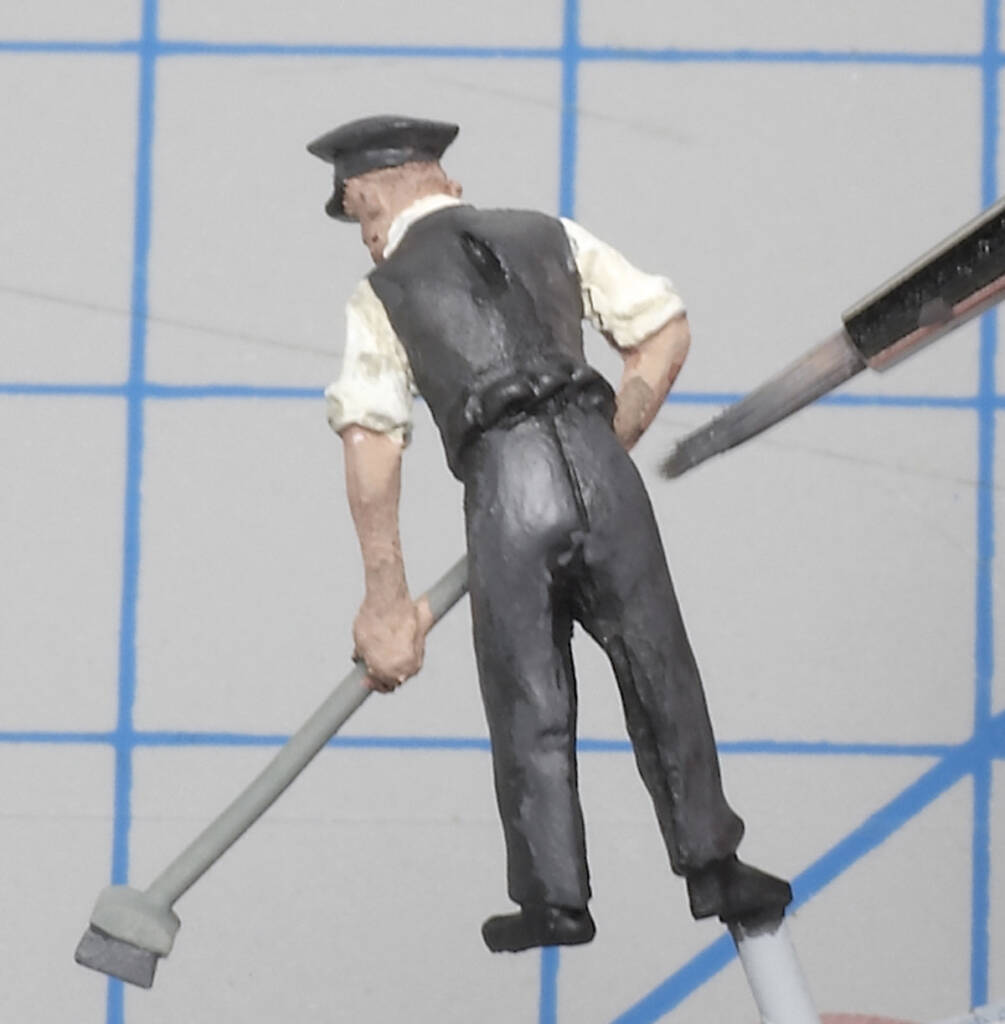 Color photo of scale figure in railroad uniform holding broom with paintbrush to the right.