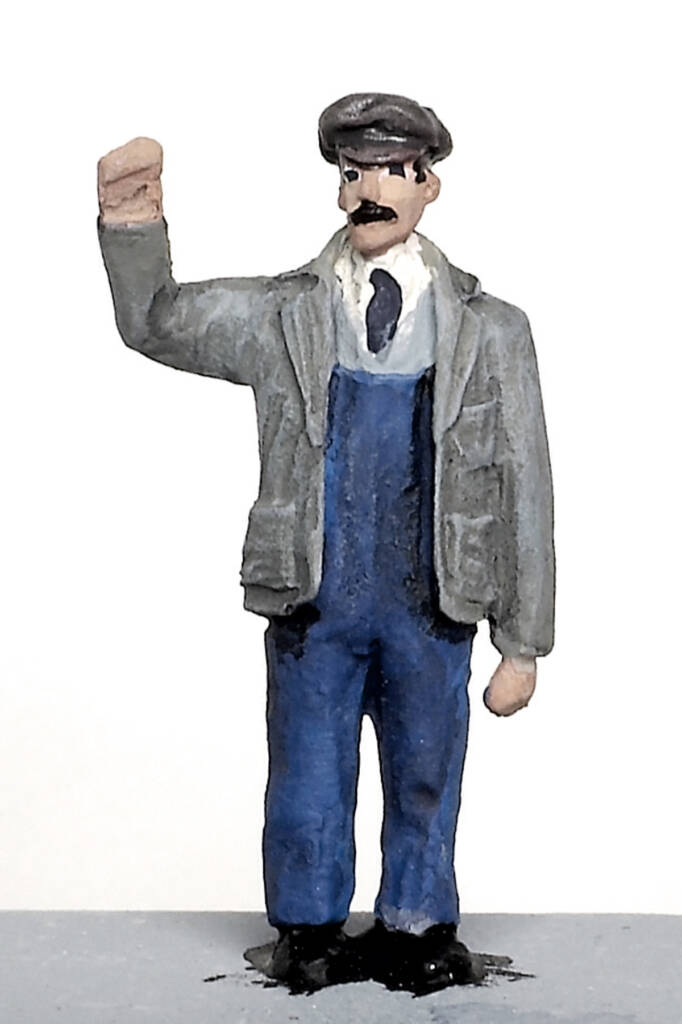 Color photo of painted scale figure with gray jacket, blue overalls, white shirt, and necktie.