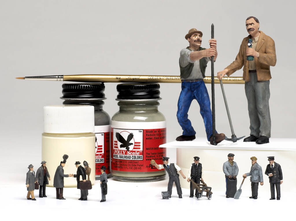 Color photo of model figures in various scales, paint bottles, and paint brush on white background.